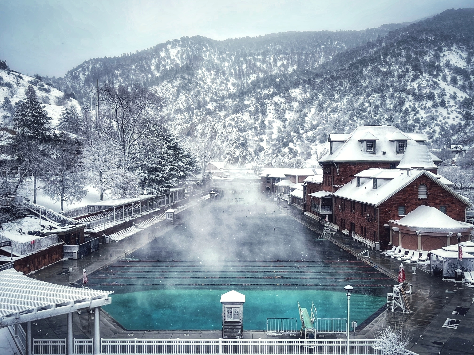 Glenwood Hot Springs Pool – winter Scenic winter view of Glenwood Hot Springs pool, surrounded by snow-covered mountains and buildings. The soothing hot springs mineral waters create a tranquil scene with steam rising, offering a serene contrast to the snowy landscape.