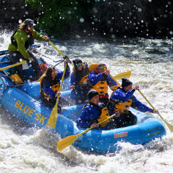 Give the gift of adventure with a gift card from Glenwood Canyon Rafting. An image capturing the adventure of a Blue Sky-branded raft navigating the Shoshone Rapids on the Colorado River. The excitement is palpable, marked by joyous smiles. The dynamic scene is intensified by water splashes that surround the raft, creating a visually striking and exhilarating composition.