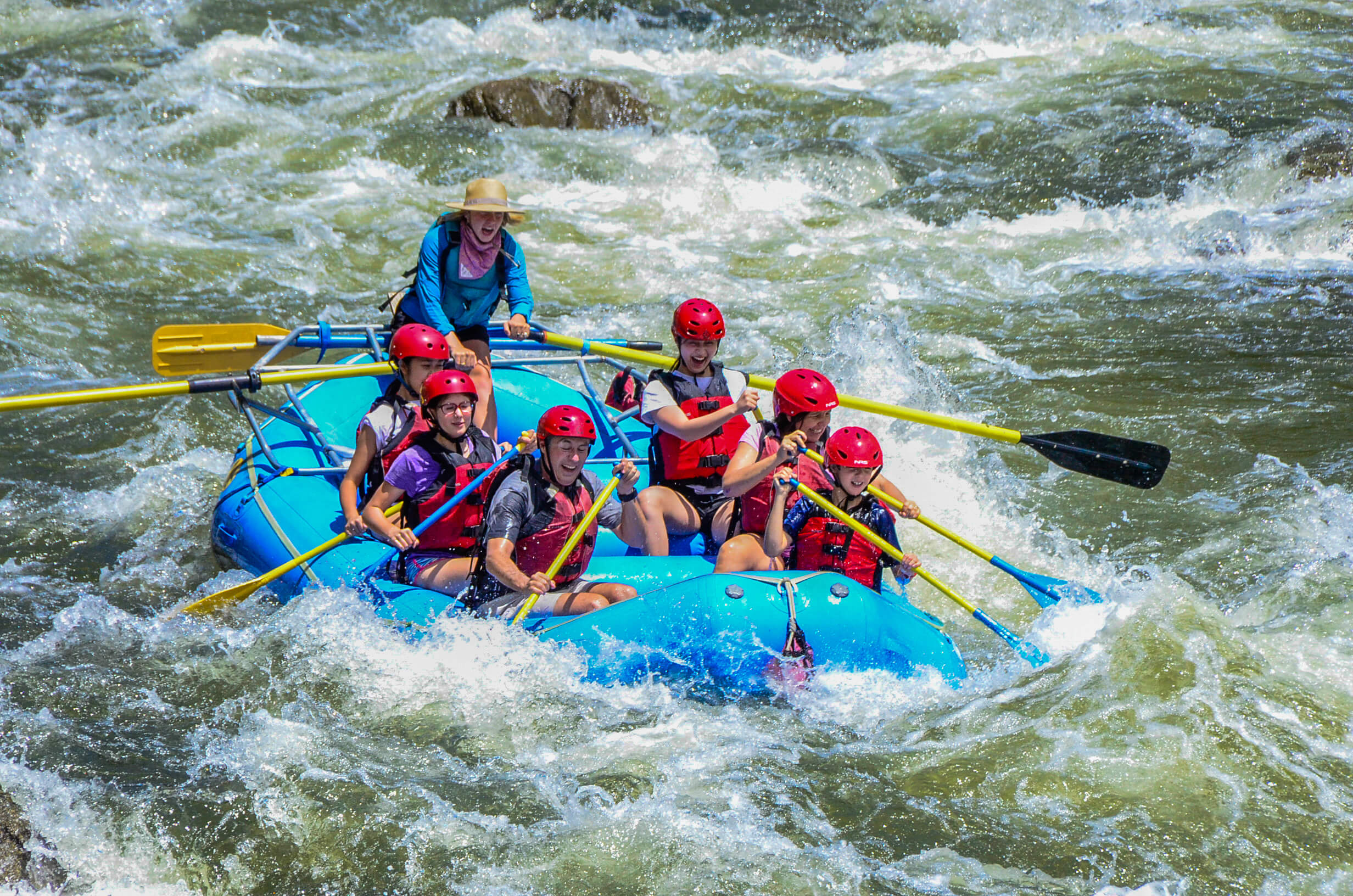An image of a boat of rafters and their guide paddling through whitewater rapids on the Colorado River.